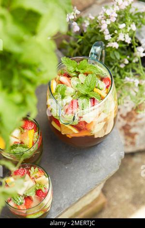 Krüge aus Pimmen mit Erdbeeren, Zitrone und Minze im Garten Stockfoto