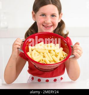 Ein Mädchen, das ein Sieb gekochter Pasta hält, 7 Jahre Stockfoto