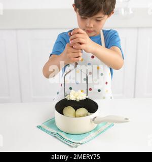 Junge Maischen Kartoffeln in einen Topf geben, 7 Jahre Stockfoto