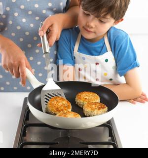 Ein Junge brät zwei Fischkuchen und Salat, 7 Jahre Stockfoto