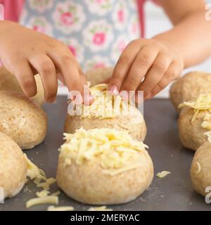 Pressen von geriebenem Käse auf ungekochte Brötchen Stockfoto