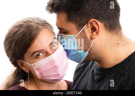 Nahaufnahme von liebevollem Freund küsst Freundin auf Wange trägt blau und rosa medizinische oder chirurgische Einweg-covid19 sars Schutzmaske als Pandemie Stockfoto