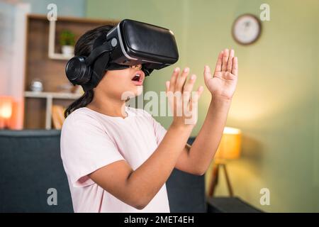 Aufgeregtes Mädchen mit Wow-Erlebnis bei der Verwendung von VR- oder Virtual-Reality-Headsets, das Objekte spürt, indem es versucht, sich in der Luft mit Metaverse zu berühren – Konzept von Stockfoto