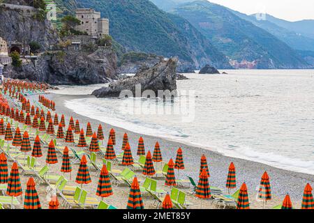 Sonnenliegen und Sonnenschirme, Felsen am Strand di Fegina, hinter dem Torre Aurora Mare, Monterosso al Mare, Cinque Terre, Ligurische Küste, Ligurien Stockfoto