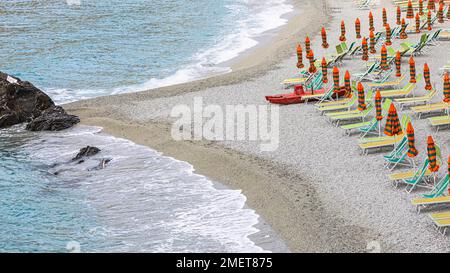 Sonnenliegen und Sonnenschirme, Felsen am Strand di Fegina, hinter dem Torre Aurora Mare, Monterosso al Mare, Cinque Terre, Ligurische Küste, Ligurien Stockfoto