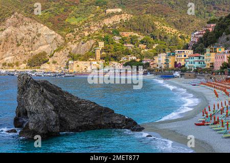 Felsbrocken, Sonnenliegen und Sonnenschirme am Strand di Fegina, hinter ihnen Ferienhäuser, die in den Hügel gebaut wurden, Monterosso al Mare, Cinque Terre Stockfoto