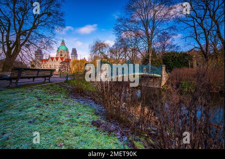 Die denkmalgeschützte Maschpark-Brücke, eine Parkbank und das neue Rathaus im Hintergrund mit blauem Himmel und verstreuten Wolken, Hannover, Lower Stockfoto