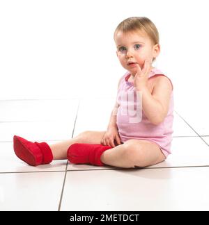 Mädchen, sitzend, mit roten Socken und rosa Oberteil, 19 Monate Stockfoto