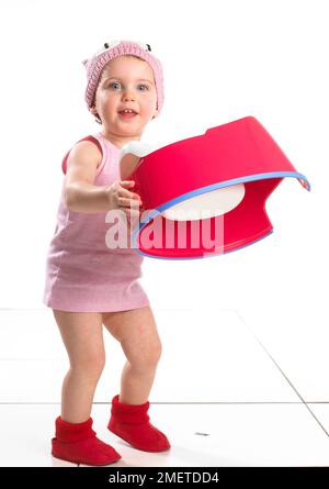 Mädchen mit roten Socken, rosa Oberteil und rosa Wollmütze mit rotem Töpfchen vorne, 19 Monate, weiß Stockfoto