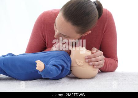 Medizinische erste-Hilfe-Untersuchungen und Behandlung des bewusstlosen Säuglings, mit Dummy, HLW, Mund vom Mund des Säuglings nehmen und sehen, ob seine Brust fällt, Kopf neigen und Kinn heben Stockfoto