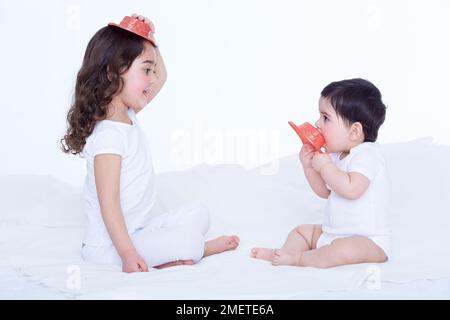 Ein kleines Mädchen (40 Wochen) und ihre Schwester (3,5 Jahre) spielen mit Plastikhüten Stockfoto