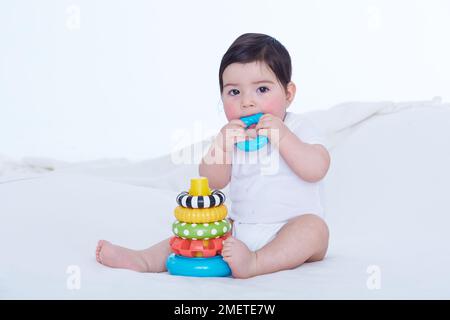 Ein kleines Mädchen (40 Wochen) beißt in einen Plastikring Stockfoto