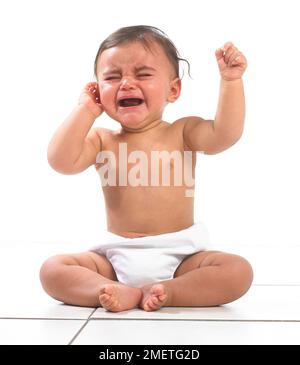Babymädchen sitzt mit Windel und weint, 7 Monate Stockfoto