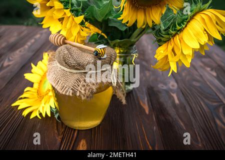 Biologischer Sonnenblumenhonig in einem durchsichtigen Glas mit Leinendeckel und einem Löffel für Honig. Sonnenblume gezüchtet, um nützlichen gesunden Honig in der Medizin zu sammeln Stockfoto