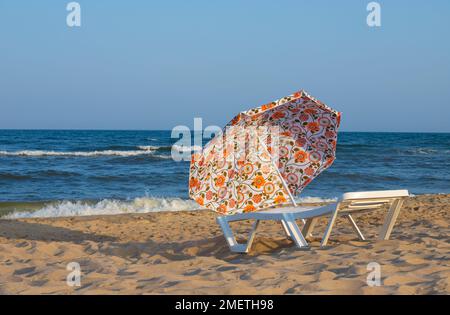 Sonnenschirm von der Sonne und Sonnenliegen sind am Strand gegen das blaue Meer, Sonnenliegen sind Handtücher. Stockfoto