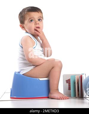 Ein Junge, der eine Weste trägt und auf einem blauen Töpfchen sitzt, 20 Monate Stockfoto