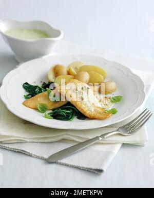 Seezungenfilets mit cremiger Pesto-Sauce auf Spinatbett, mit Basilikumblättern und gekochten Kartoffeln Stockfoto