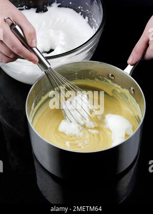 Käse-Soufflés zubereiten, Eiweiß zur gekühlten Sauce hinzufügen und Mischung mit Schneebesen schlagen Stockfoto