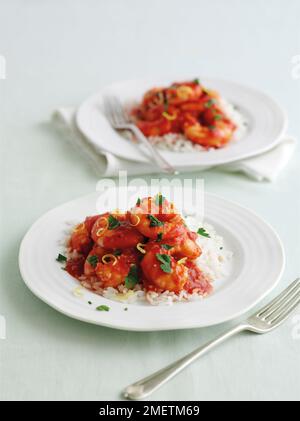 Knoblauchgarnelen mit Tomatensoße, garniert mit gehackter Petersilie und Zitronenschale, serviert auf einem Reisbett Stockfoto