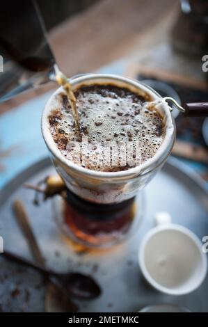 Caffe Touba, gieße heißes Wasser in den Kaffee und fließe es durch ein Tuch in die Glaskanne Stockfoto