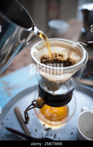 Caffe Touba, gieße heißes Wasser in den Kaffee und fließe es durch ein Tuch in die Glaskanne Stockfoto