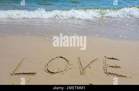 Inschrift Liebe auf den Sand gemalt. Konzept wahrer und ehrlicher romantischer Gefühle. Spa-Roman am Meer. Stockfoto