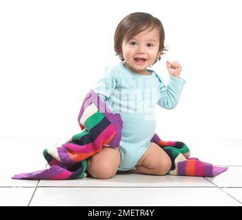 Ein kleiner Junge kniet mit einer bunten Decke um ihn herum Stockfoto