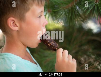 Der Junge isst Eiscreme auf einem Stock in Schokolade. Stockfoto