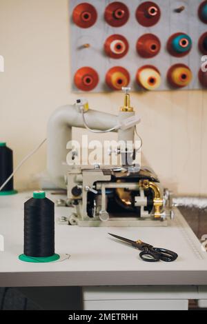 Gewindespule. Bunte, an der Wand hängende Gewindespindeln in der Textil- und Textilherstellung. Nähmaschine auf dem Tisch. Anpassung und Stockfoto