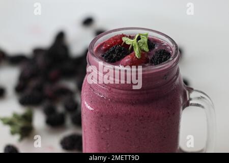 Gemischter Beerensaft. Dicker, cremiger Smoothie aus frischen Erdbeeren und Maulbeeren in Mandelmilch. Serviert in einem Smoothie-Glas. Aufnahme auf weißem Hintergrund Stockfoto