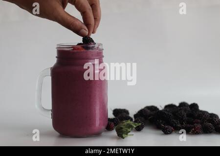 Gemischter Beerensaft. Dicker, cremiger Smoothie aus frischen Erdbeeren und Maulbeeren in Mandelmilch. Serviert in einem Smoothie-Glas. Aufnahme auf weißem Hintergrund Stockfoto