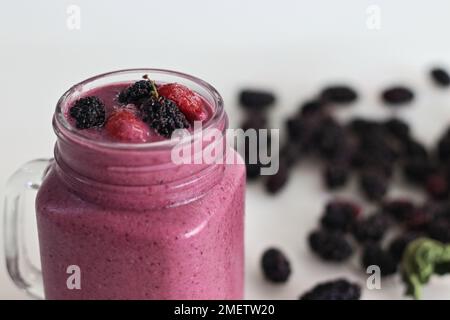 Gemischter Beerensaft. Dicker, cremiger Smoothie aus frischen Erdbeeren und Maulbeeren in Mandelmilch. Serviert in einem Smoothie-Glas. Aufnahme auf weißem Hintergrund Stockfoto