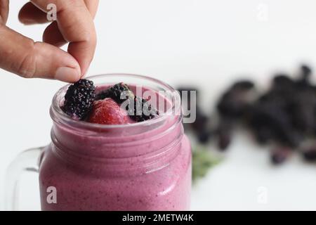 Gemischter Beerensaft. Dicker, cremiger Smoothie aus frischen Erdbeeren und Maulbeeren in Mandelmilch. Serviert in einem Smoothie-Glas. Aufnahme auf weißem Hintergrund Stockfoto