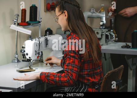 Eine Frau näht in der Fabrik eine professionelle Nähmaschine an. Personalisieren Sie Accessoires aus umweltfreundlichem Leder. Fertigungskonzept. Frauen, die in Leder arbeiten Stockfoto