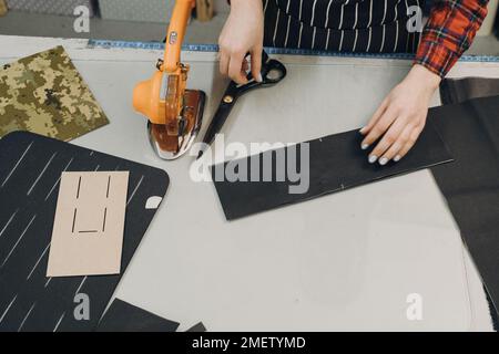 Näherin bei der Arbeit. Schneidewerkstoff. Frau, die mit geschnittenem Textil am Tisch steht und an einem Design arbeitet. Draufsicht, Nahaufnahme mit Kopierbereich Stockfoto