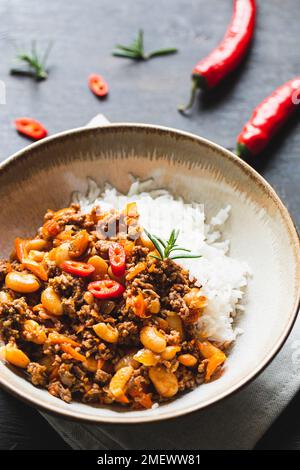 Chili Con Carne in Schüssel auf dunklem Hintergrund. Mexikanische Küche. Chili con Carne - Hackfleisch und Gemüse Eintopf in Tomatensauce. Draufsicht Stockfoto