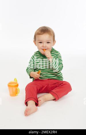 Kleiner Junge in grün gestreiftem Oberteil mit Becher (Modellalter – 22 Monate) Stockfoto