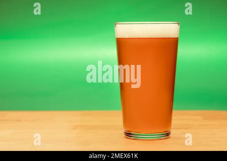 Volles Shaker Pint Glas Amber Ale oder Bier auf Holztisch mit grünem Hintergrund Stockfoto