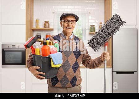 Ein älterer Mann hält einen Eimer mit Reinigungsmitteln und einen Bodenwischtuch in einer Küche Stockfoto