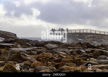 Eine Gruppe von Menschen traut sich kaltem, windigen Wetter, um die Lücke von einer freitragenden Aussichtsplattform zu betrachten, die von Felsen in der Nähe von Albany in Westaustralien unterstützt wird Stockfoto