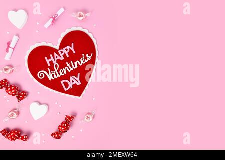 Pinkfarbener Valentinstag mit Herz, Text „Happy Valentine's Day“, Süßigkeiten und Herzverzierungen und Kopierbereich Stockfoto