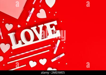 Dekoration zum Valentinstag mit Liebestexten, Herzschmuck und Streuseln auf rotem Hintergrund mit Kopierbereich Stockfoto