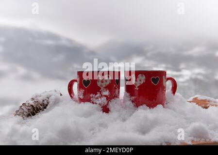 Zwei rote Tassen mit Herzform im Schnee- und Berghintergrund - valentinskonzept Stockfoto