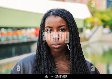 Nahaufnahme von einer ernsthaften afroamerikanischen Frau mit Zöpfen, die vor der Kamera nachdenklich aussehen. Vorderansicht eines jungen Afro-Mädchens. Zeitlupe. Hochwertiges Foto Stockfoto