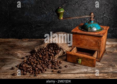 Alte Kaffeemühle mit Esparto-Grasbeutel und Kaffeebohnen auf einem rustikalen Holztisch. Stockfoto