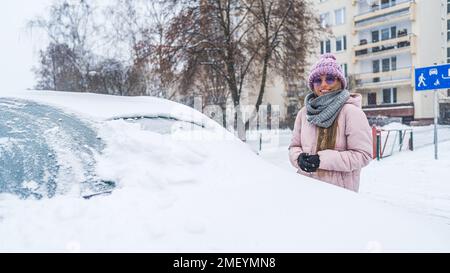 Eine Frau mit Sonnenbrille, die neben dem Auto stand und unter dem Schnee begraben wurde. Hochwertiges Foto Stockfoto