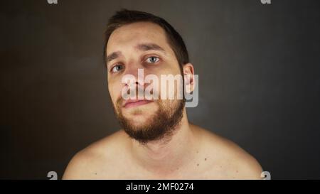 Der Typ will sich nicht rasieren. Nahaufnahme eines jungen, gutaussehenden europäischen Mannes, der im Badezimmer steht. Ein gesunder bärtiger Mann schaut in die Kamera Stockfoto