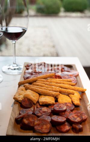 Holzteller mit spanischen Tapas, Choriso-Wurst, Lomo iberico en Brotstangen, serviert mit einem Glas Rotwein, aus nächster Nähe Stockfoto