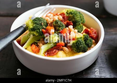 Brokkoli und Bohnen auf Polenta mit getrockneten Tomaten und Paprika. Stockfoto
