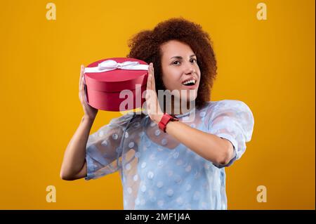 Junge, lockige Frau mit einer Geschenkbox in den Händen Stockfoto